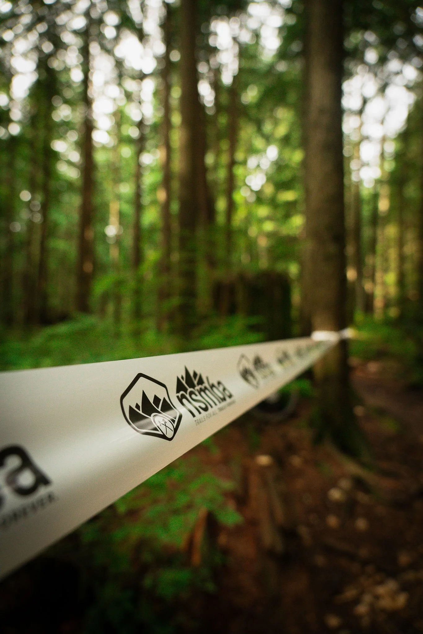 A close-up photo of a trail marking tape in a forest, with the NSMBA trail logo.