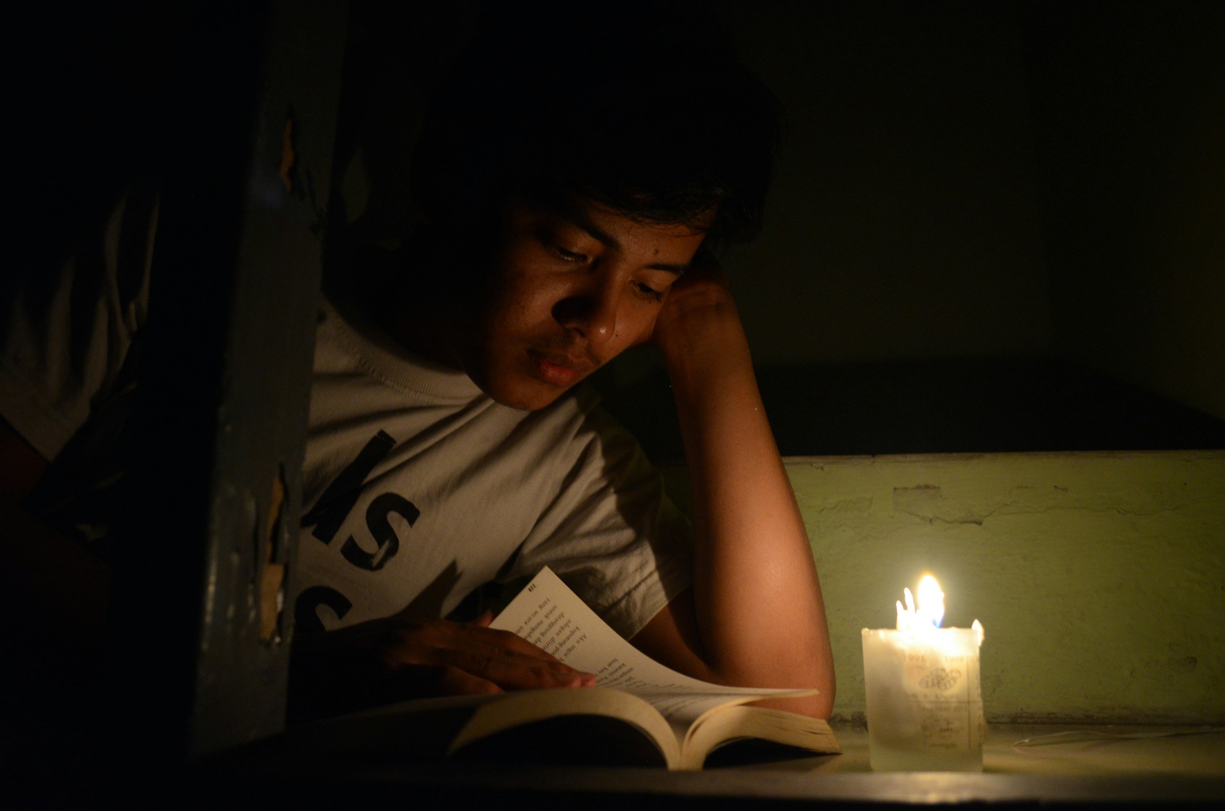 Someone reading a book by candlelight against a dark background.