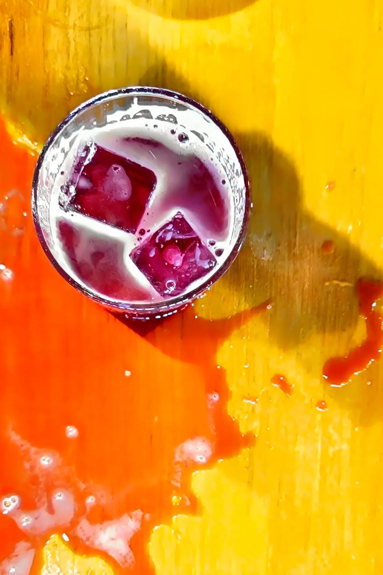 A glass of dark-colored beverage with ice cubes on a colorful orange and yellow surface.