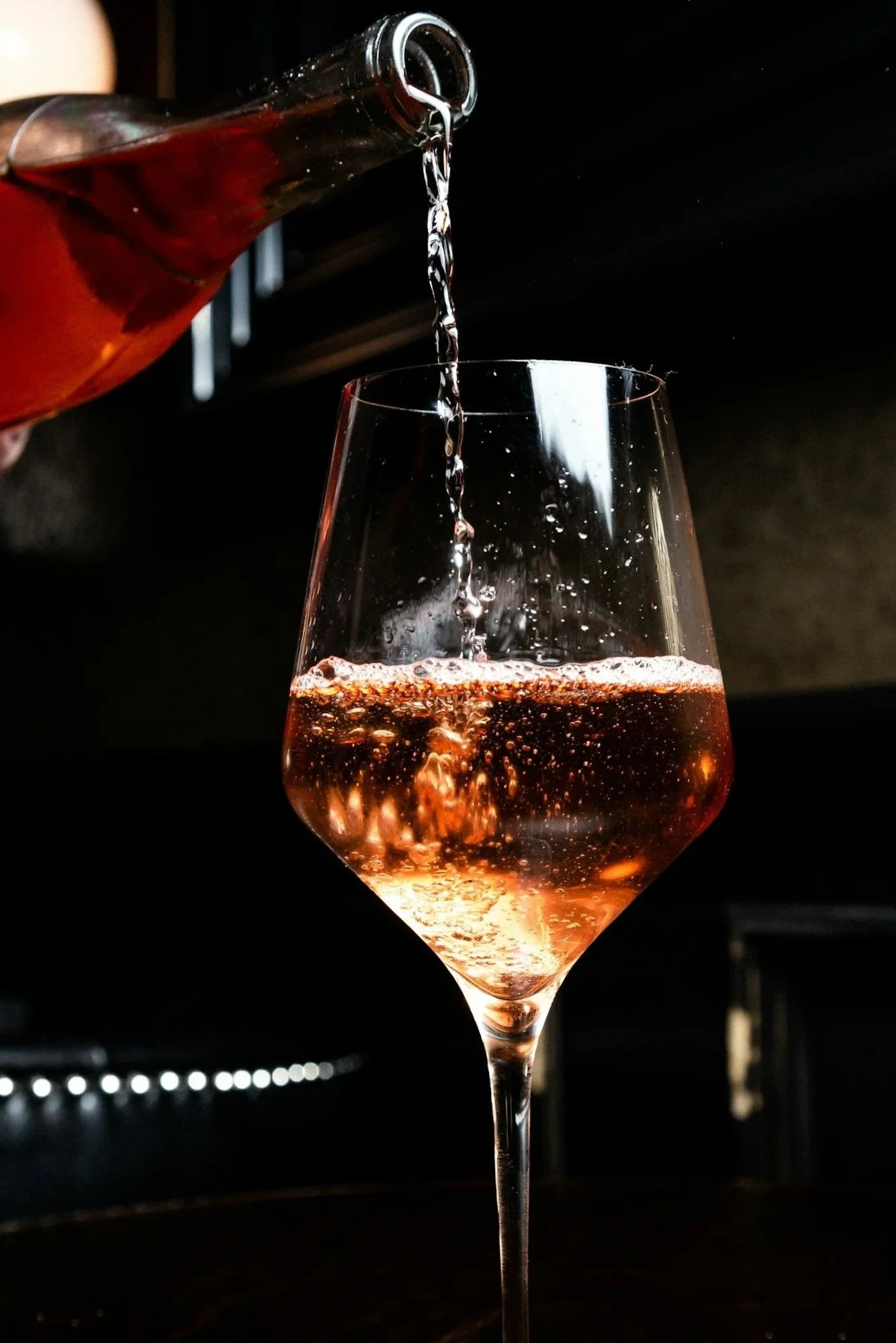 A glass of rosé wine being filled from a bottle against a dark background.