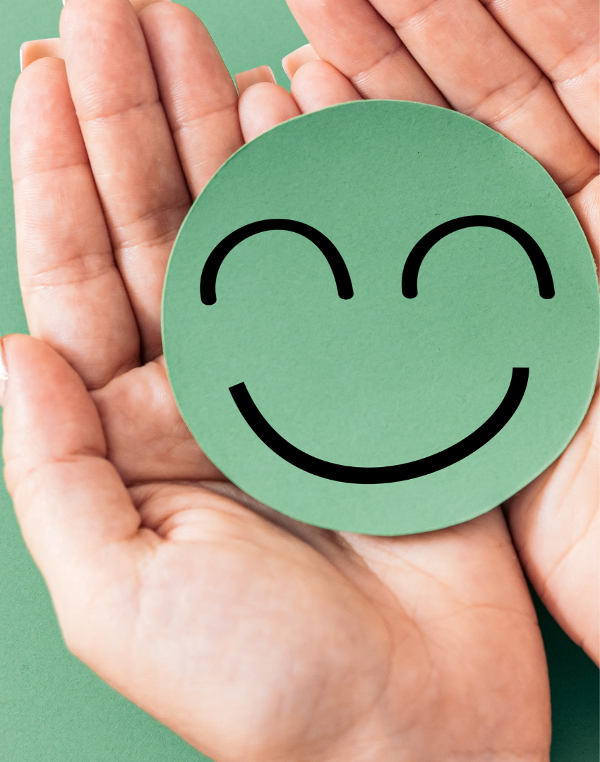 A person holding a green circular paper with a black smiling face, with a green background.