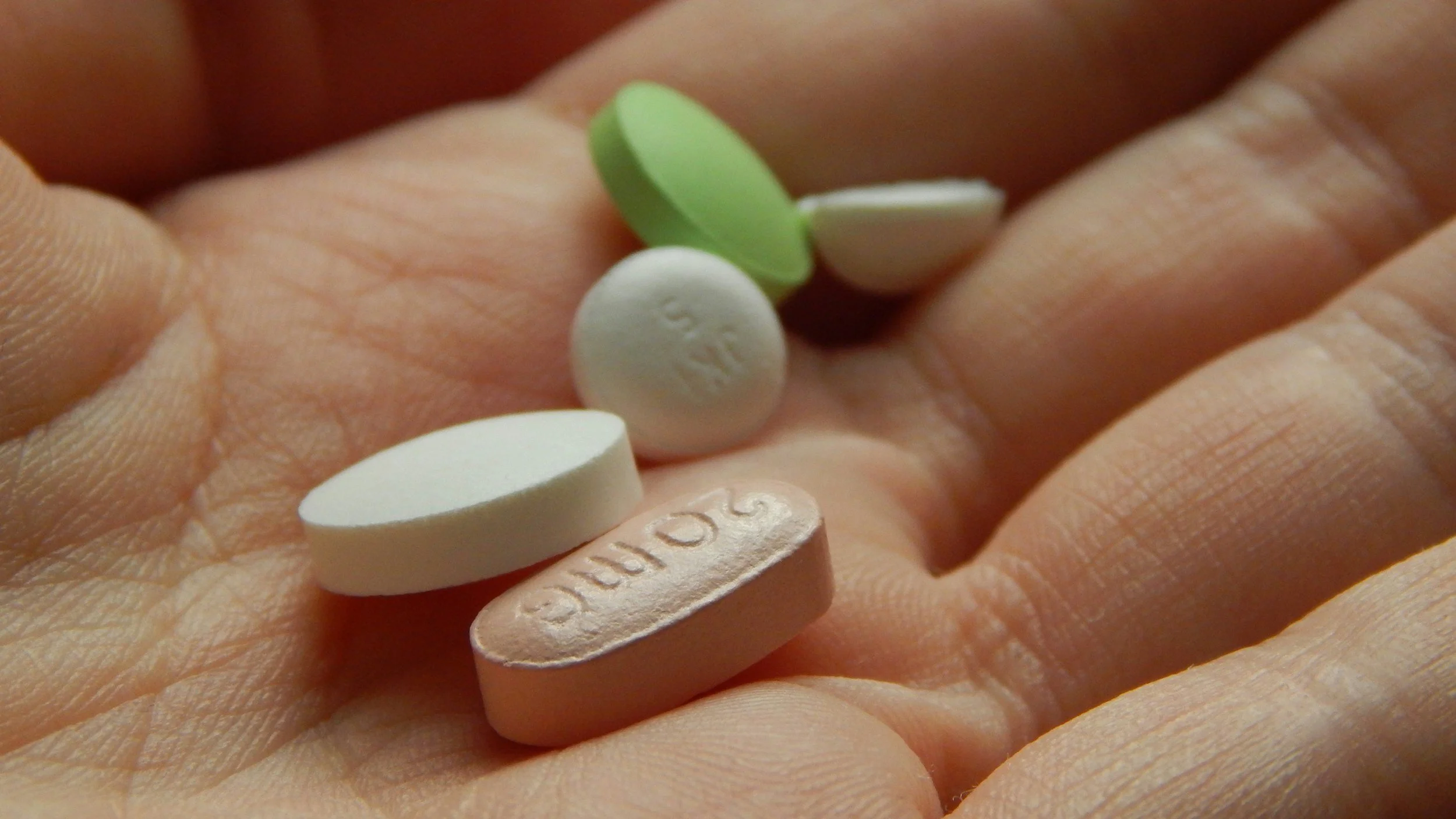 Close-up of a person's open hand holding multiple prescription pills of different shapes and colors.