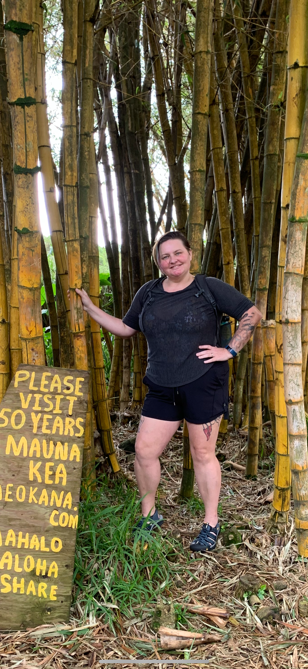 Person standing in a bamboo forest next to a wooden sign with yellow text.