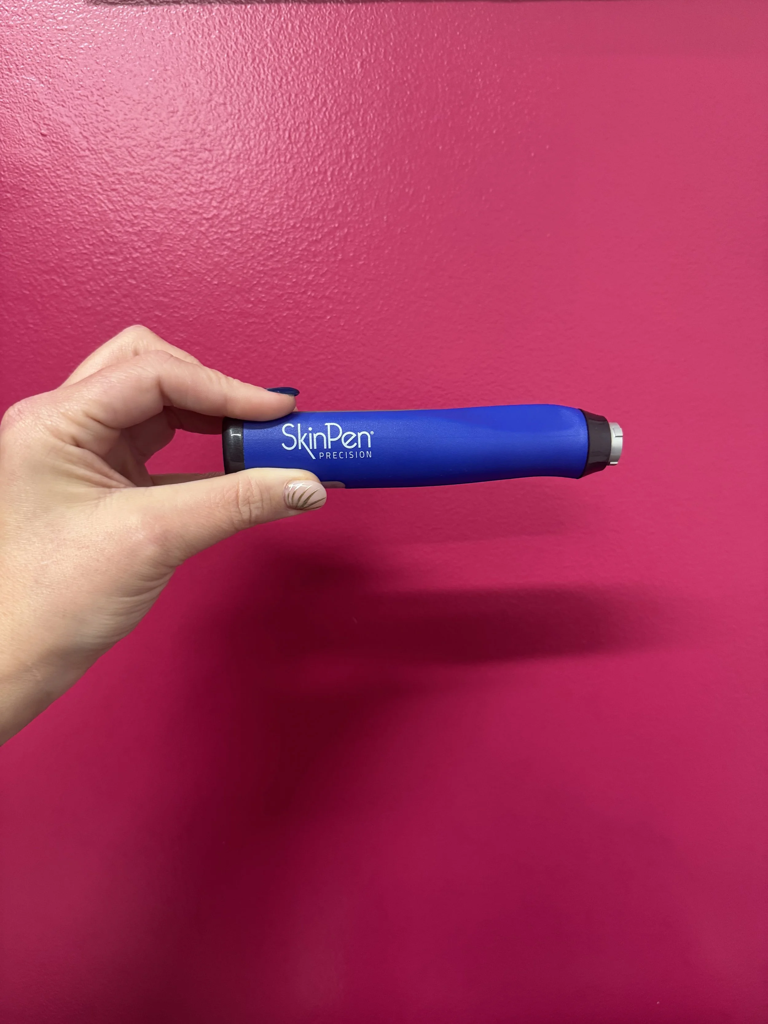 A hand holding a blue SkinPen Precision device against a pink textured wall.
