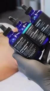 Three blue bottles of medical or skincare serum with droppers, held by a gloved hand.