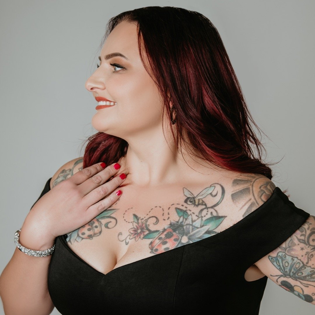 Woman with colorful tattoos wearing black dress, smiling and looking sideways