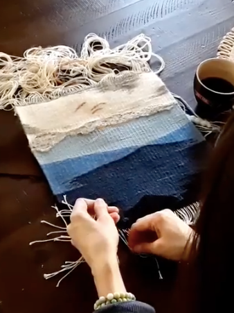 Person weaving a flag or cloth on a loom with yarn, with a cup of coffee nearby.
