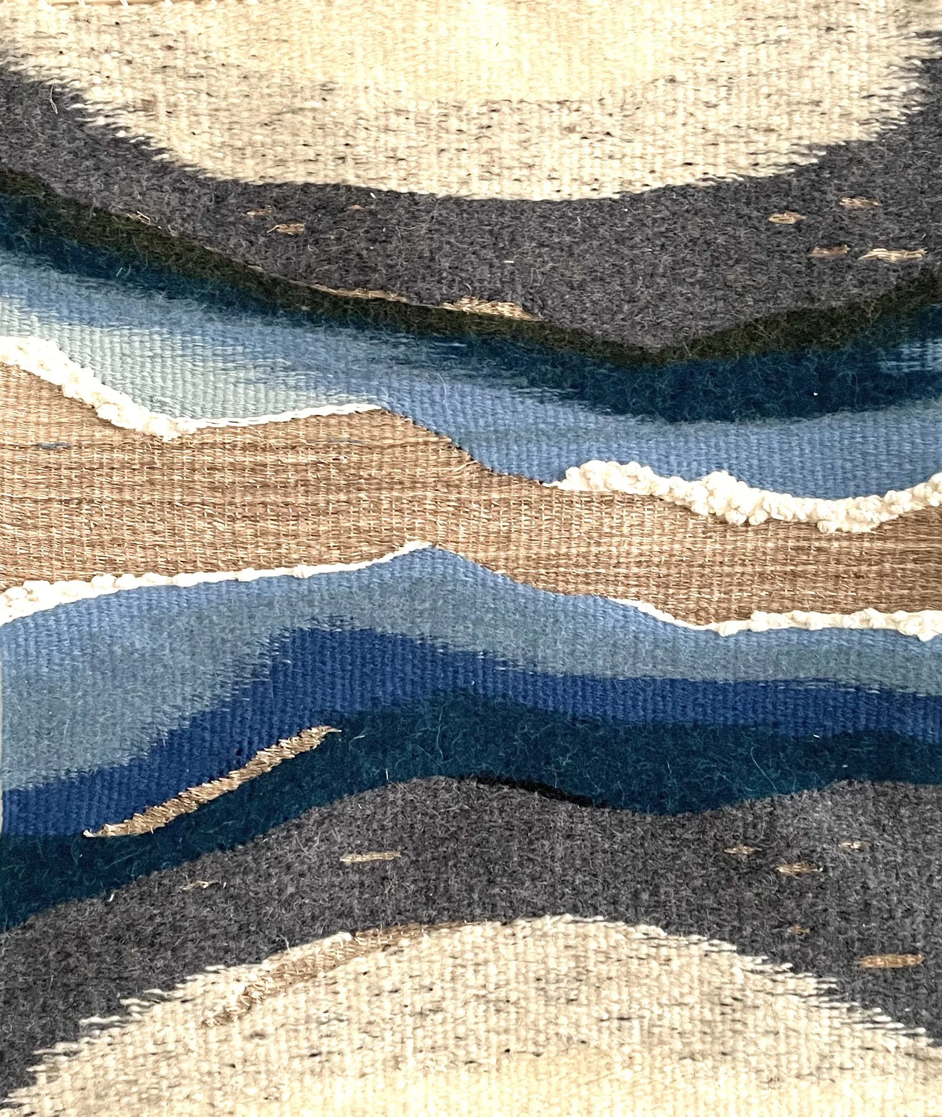 Close-up of a textured, multicolored rug with wavy patterns in beige, black, blue, and brown.