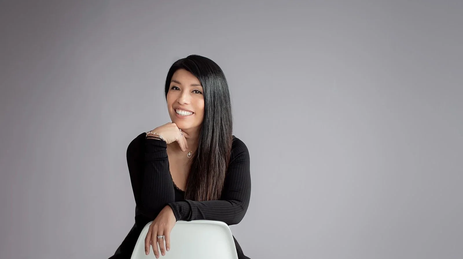 Tanja Paola Hasbi von Unique Journey, sitzend und lächelnd vor grauem Hintergrund