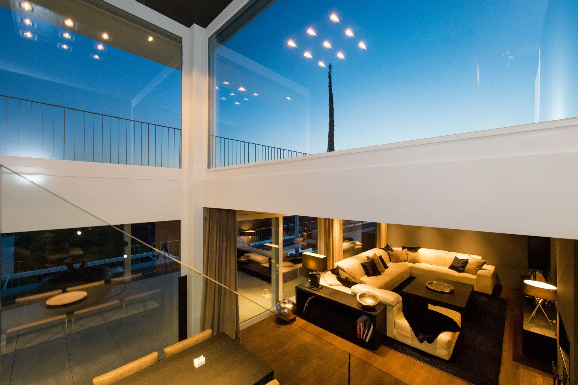 Innenansicht eines modernen mehrstöckigen Wohnzimmers mit Panorama-Fenstern, stilvoller Einrichtung und stimmungsvollem Licht – Beispiel moderner Immobilienfotografie von eDESIGN SOLUTIONS.
