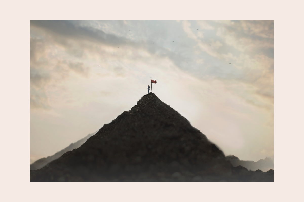 A woman standing beside a flag at the summit of a mountain, symbolising reclaiming her life and choosing her own path.