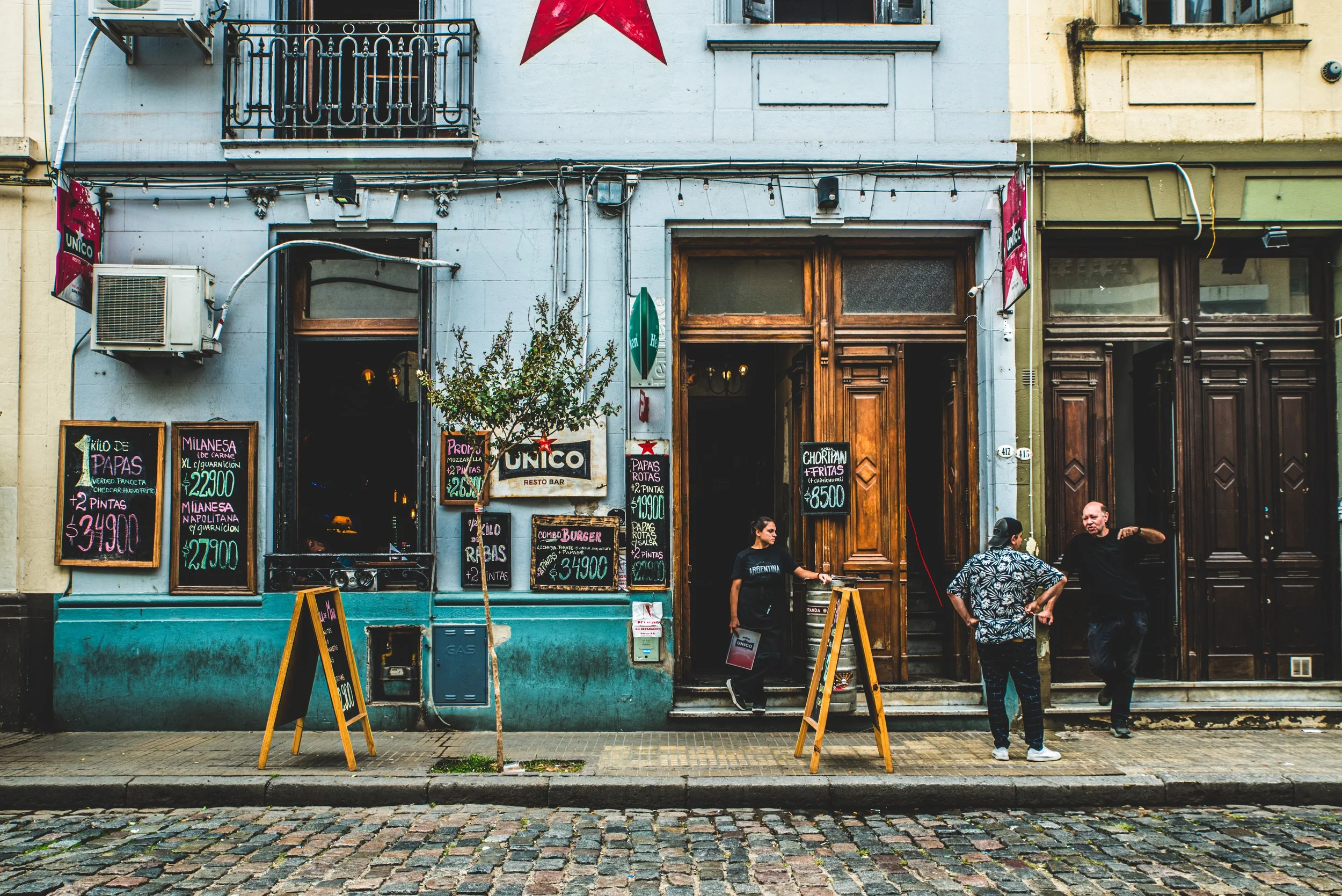 Casa de arquitectura clásica argentina con un café en la planta baja, dos mozos y una señal de tránsito en la vereda, representando el regreso gradual a la vida cotidiana al recuperar la motivación.