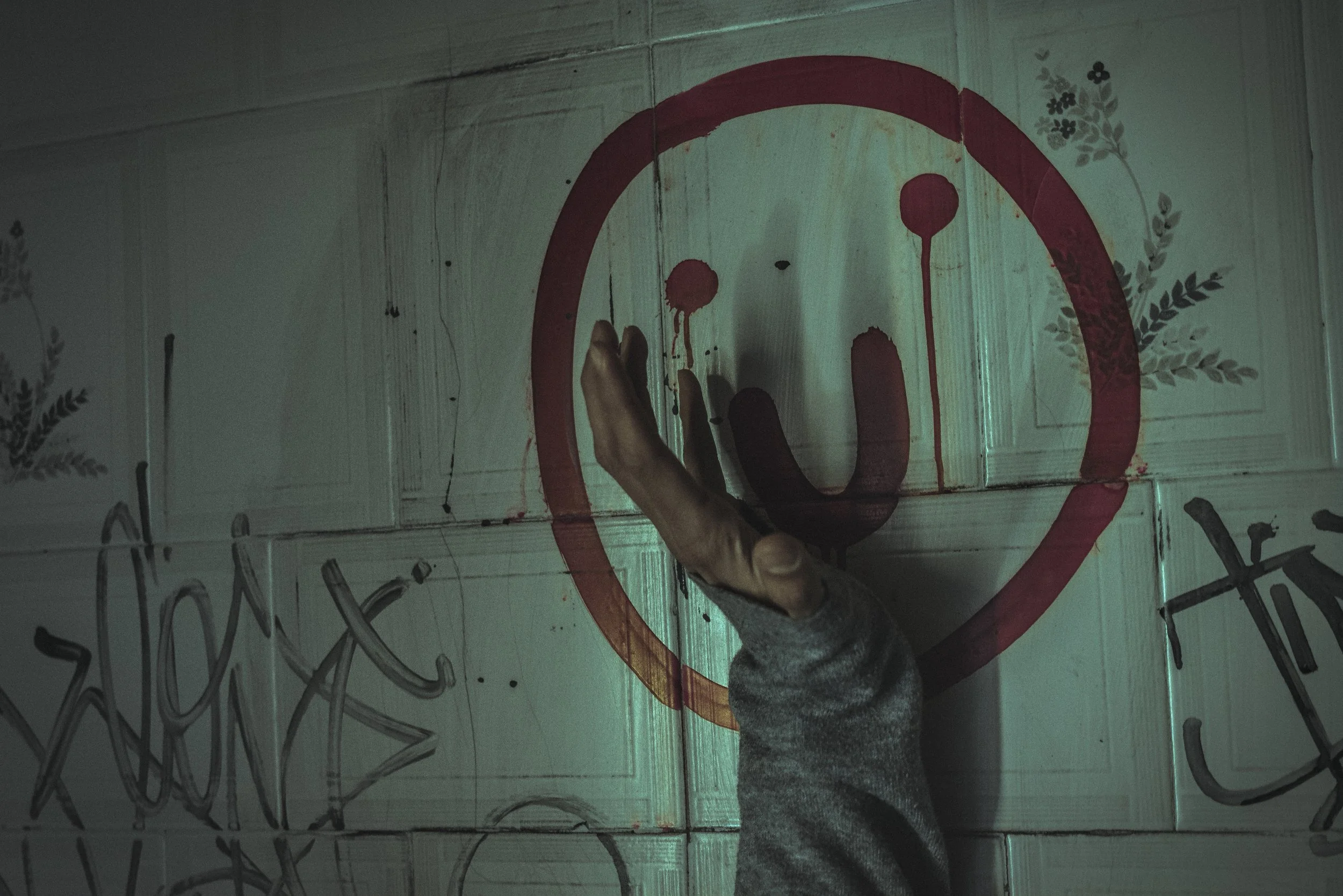 Mano apoyada en la pared de un baño abandonado junto a una carita sonriente pintada, representando la búsqueda de alivio frente a la ansiedad cuando apa