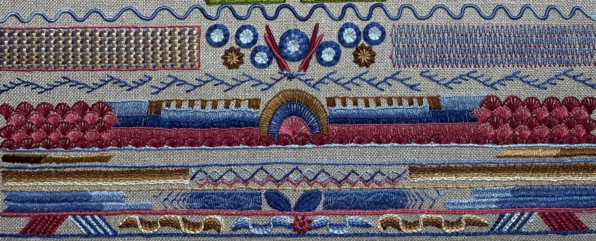 Close-up of colorful embroidered textile with patterns in red, blue, gold, and pink, featuring geometric and floral designs.