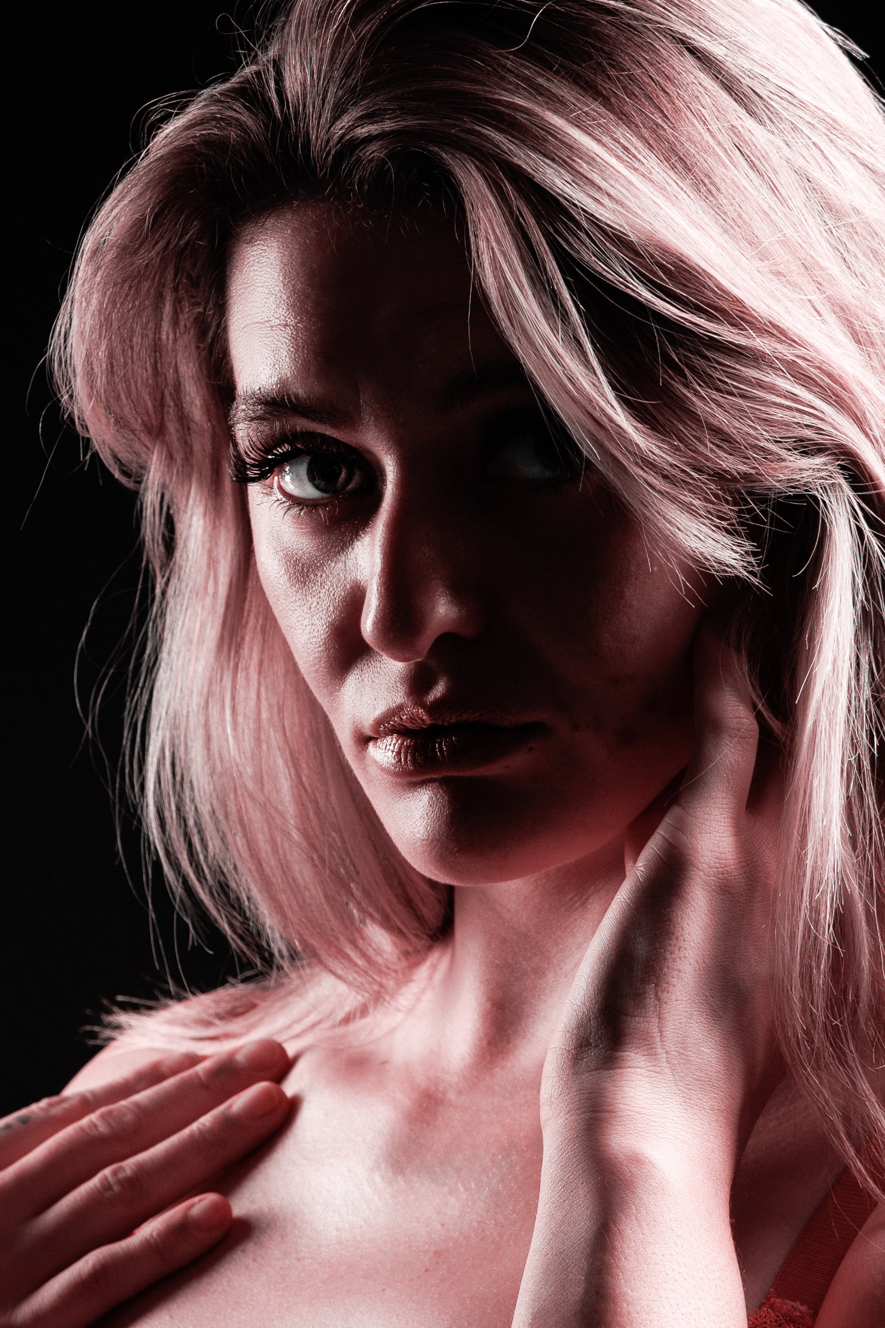 A woman with pink hair and blue eyes posing against a black background.