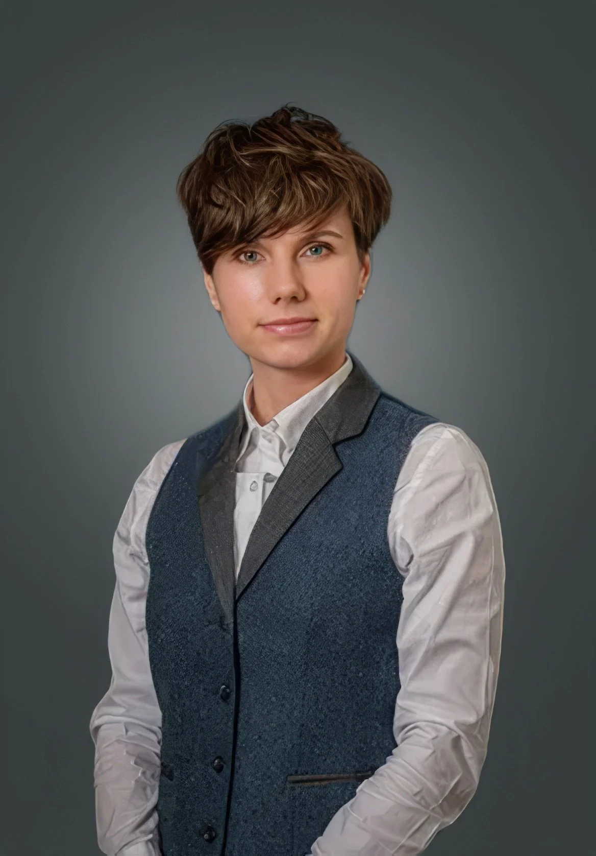 Person with short hair wearing a white shirt and dark vest, posing against a gray background.
