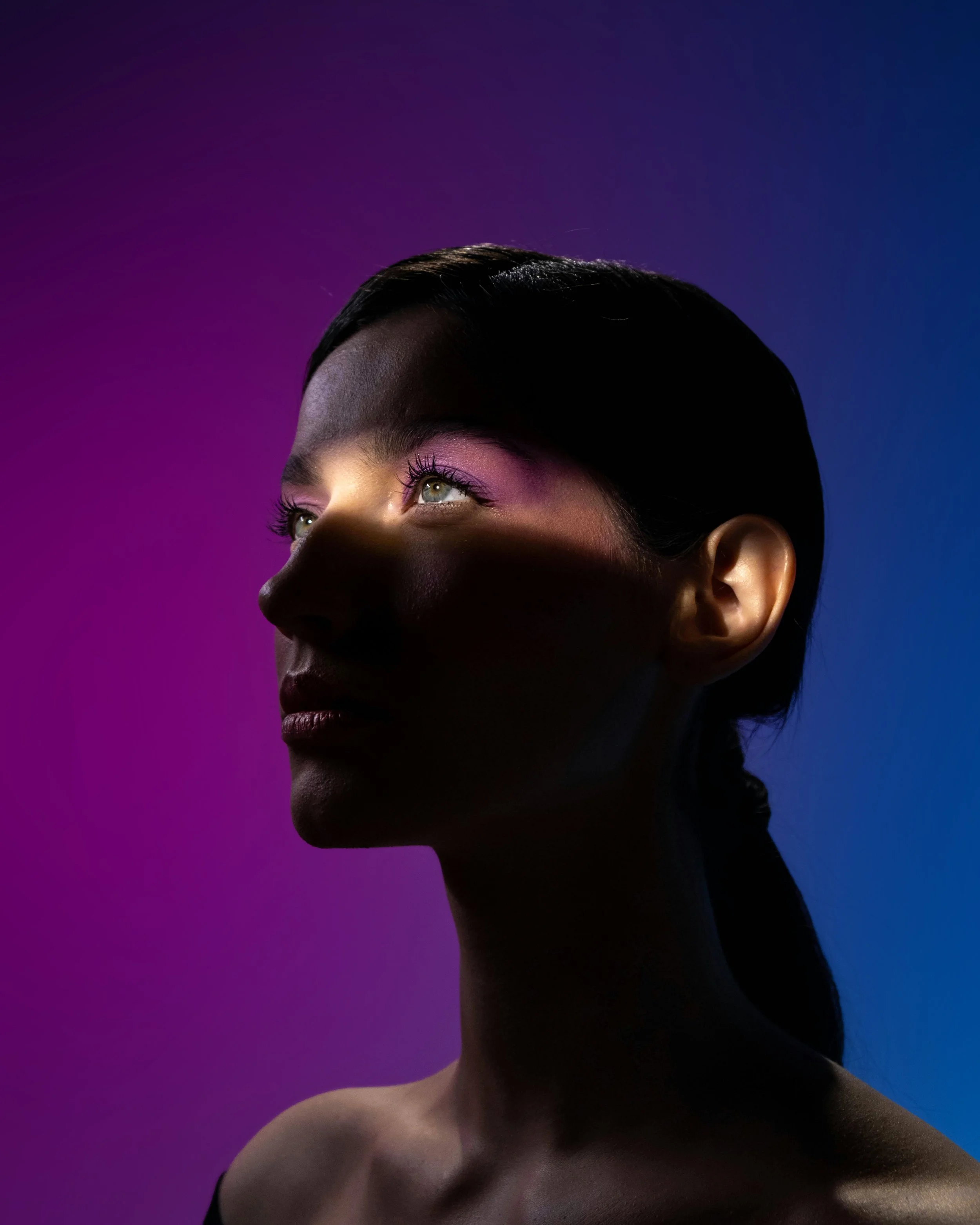 A portrait of a woman with dark hair, light makeup, and illuminated eyes, against a background with a gradient from purple to blue.