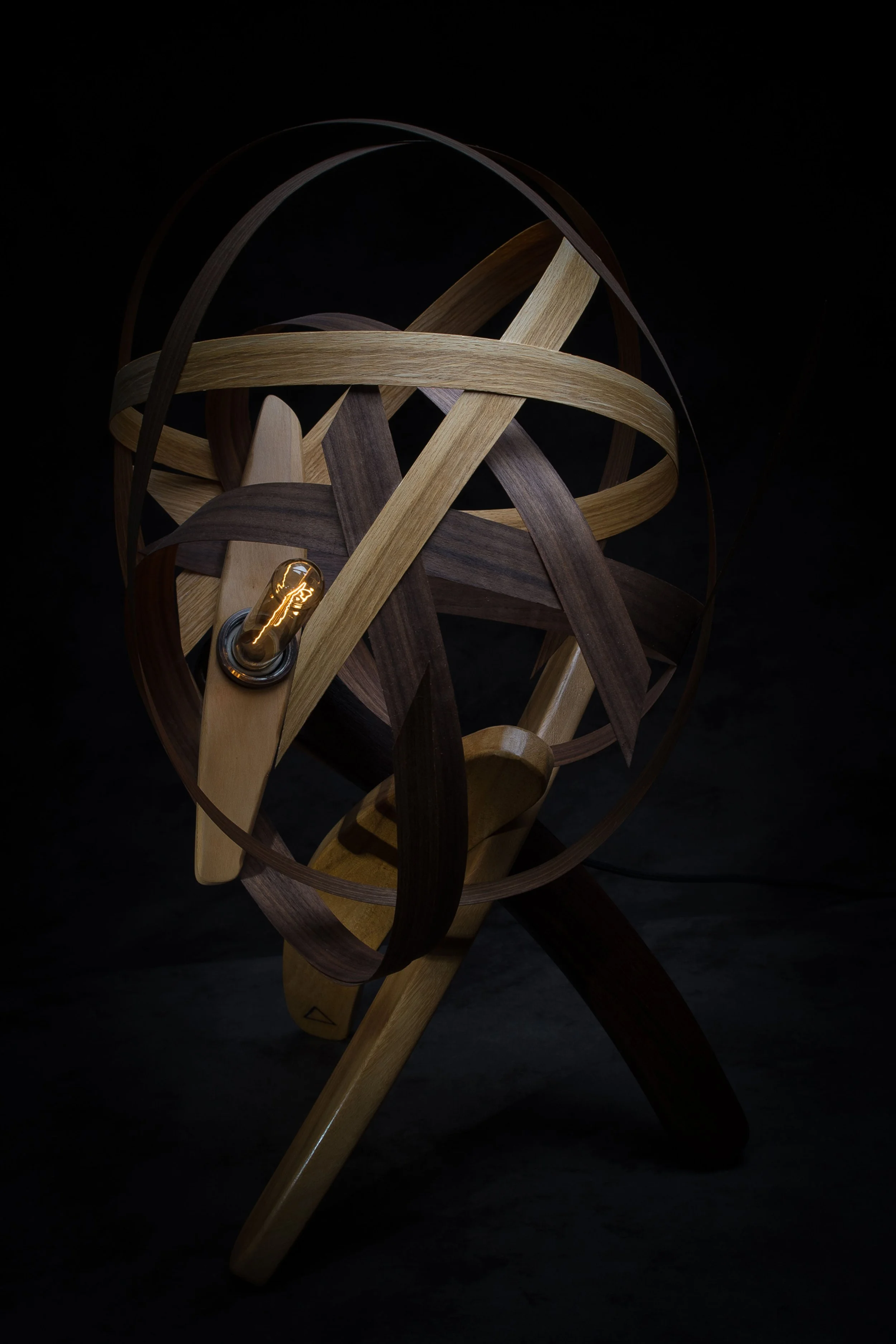 Lampe sculpturale en bois entrelacé avec ampoule visible, sur fond sombre.