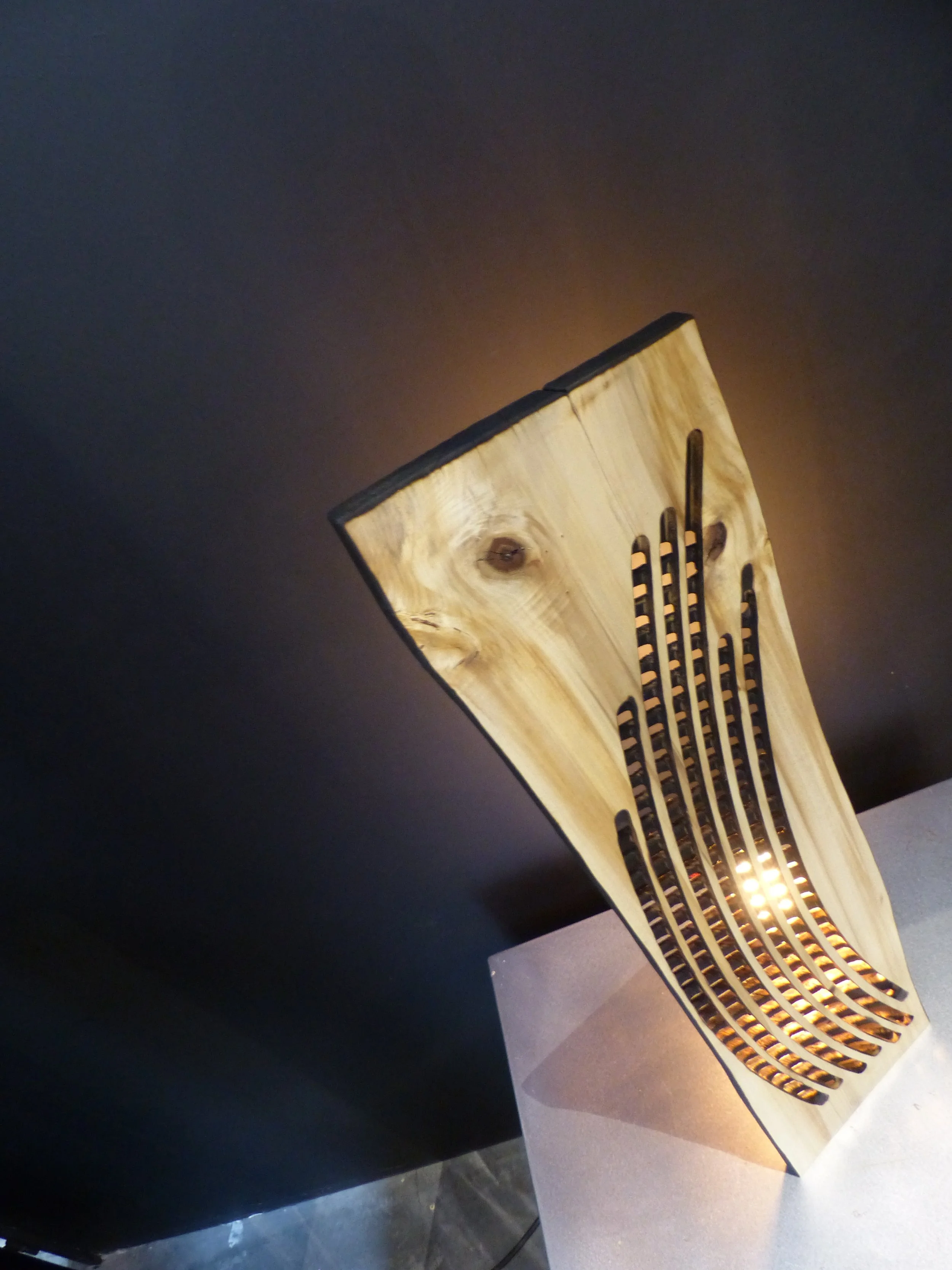 Lampe design en bois avec motif découpé, éclairage doux sur fond sombre.
