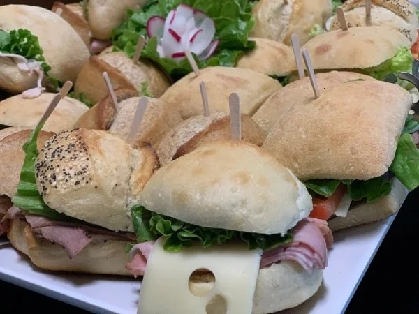 Close up shot of small sandwiches on a white tray with a carved radish flower garnish.