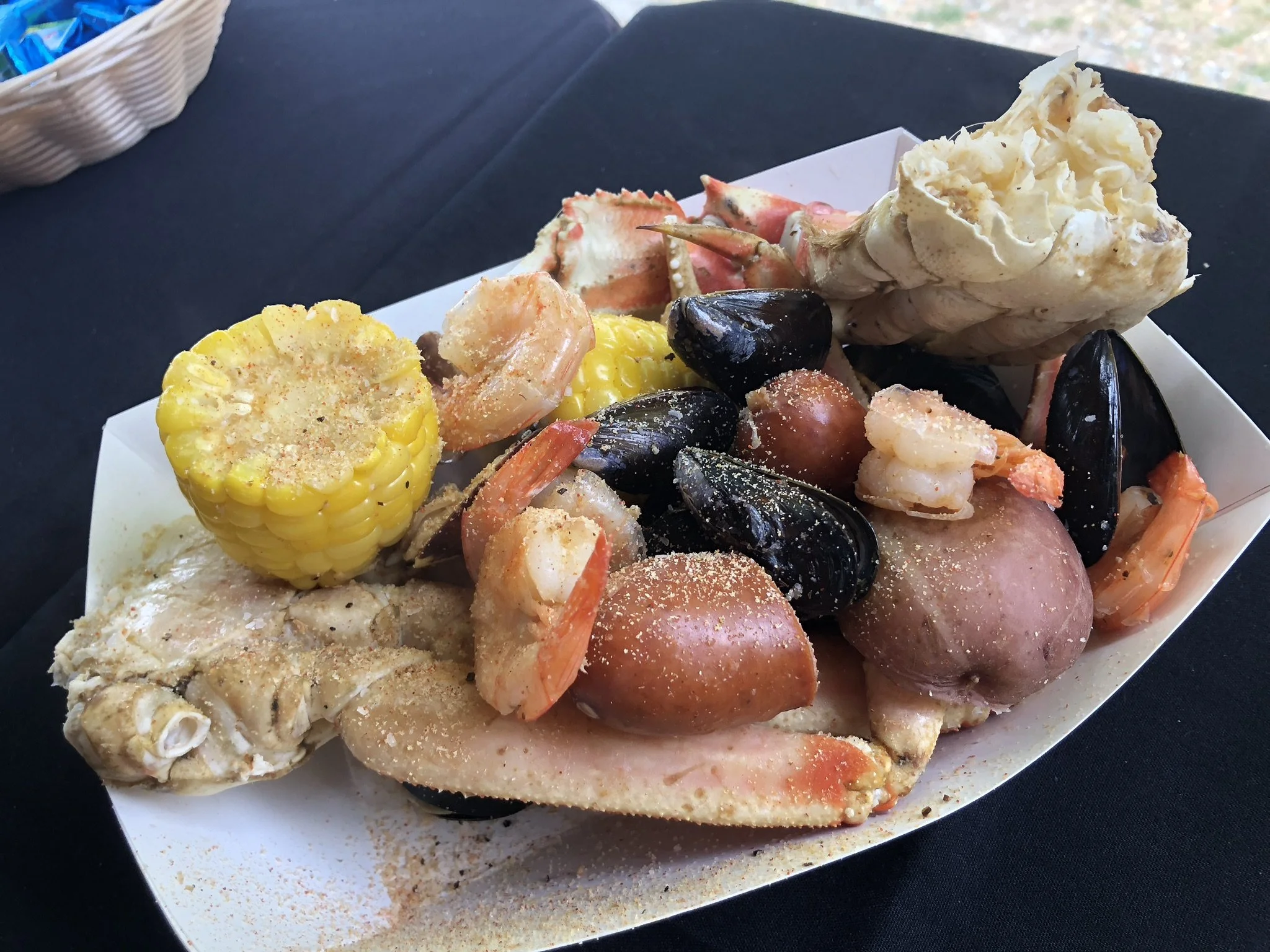 Seafood boil with corn on the cob, shrimp, crab, mussels, potatoes, and corn, served on a white boat-shaped platter.