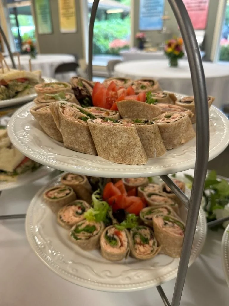 A two-tiered tray filled with pinwheel wraps garnished with a flower cut tomato