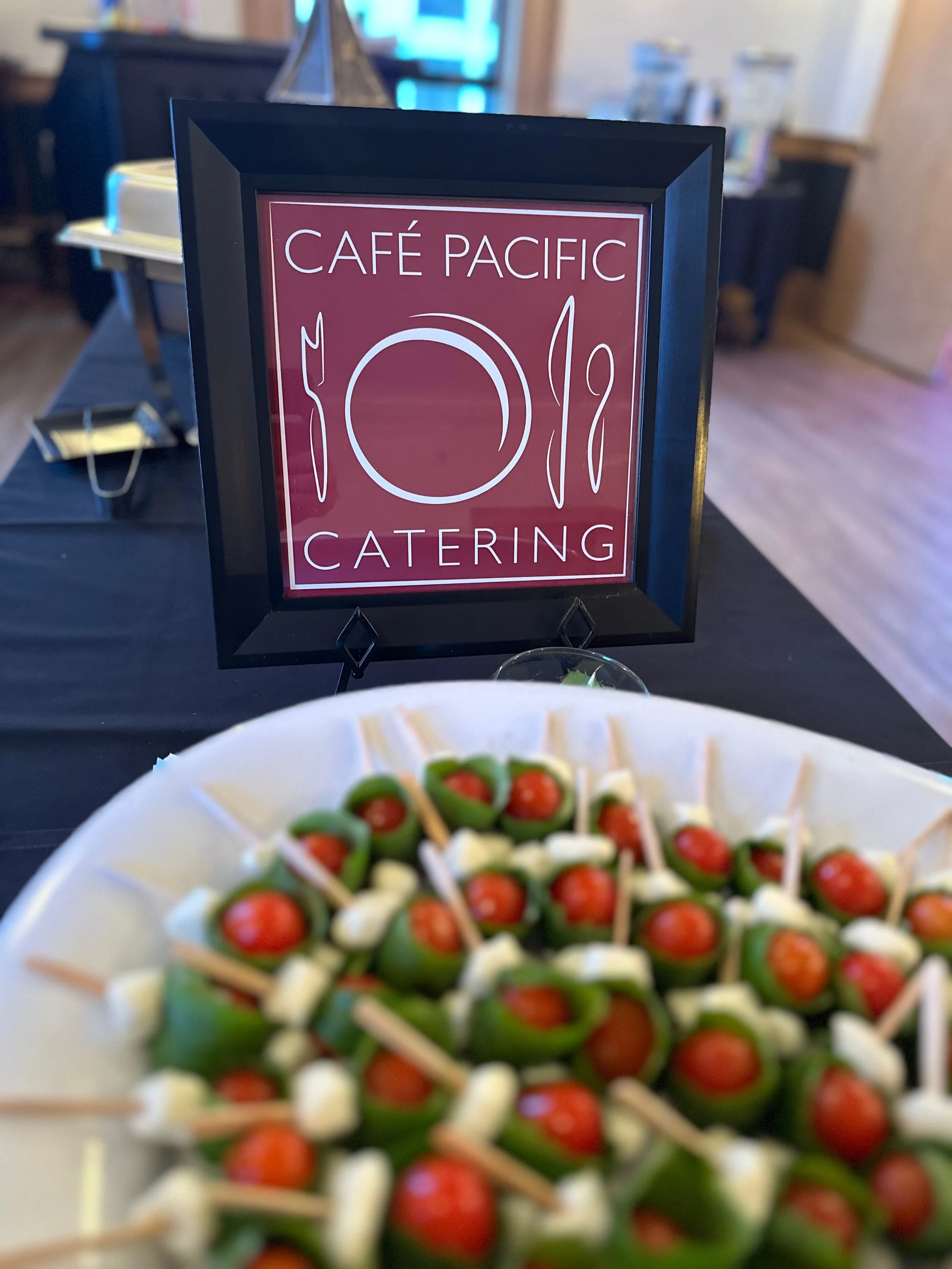 Appetizer platter with green stuffed peppers filled with cherry tomatoes and cheese, in front of a sign for Café Pacific Catering.