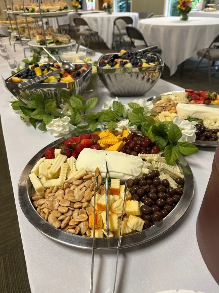 A tray of cheeses, nuts, strawberries, and grapes at the start of a buffet line