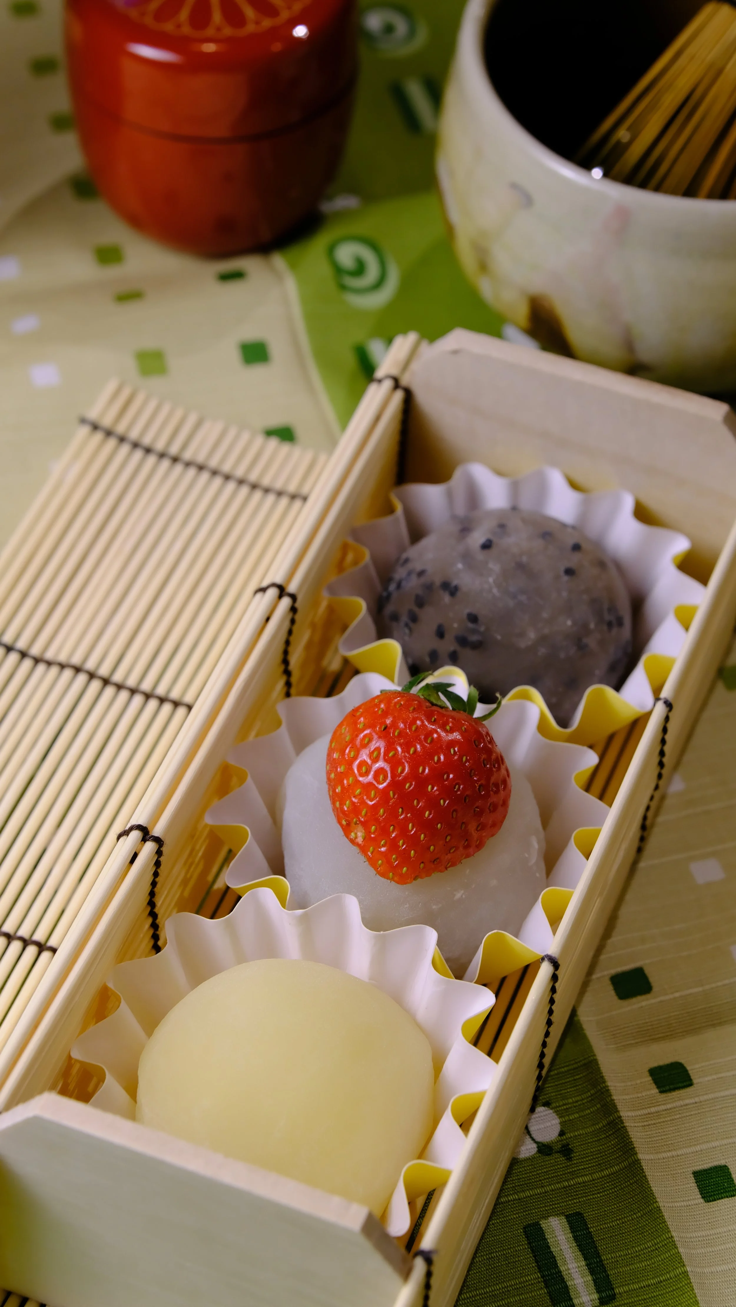 Assorted Japanese mochi ice creams with a fresh strawberry on top, displayed in a bamboo box.