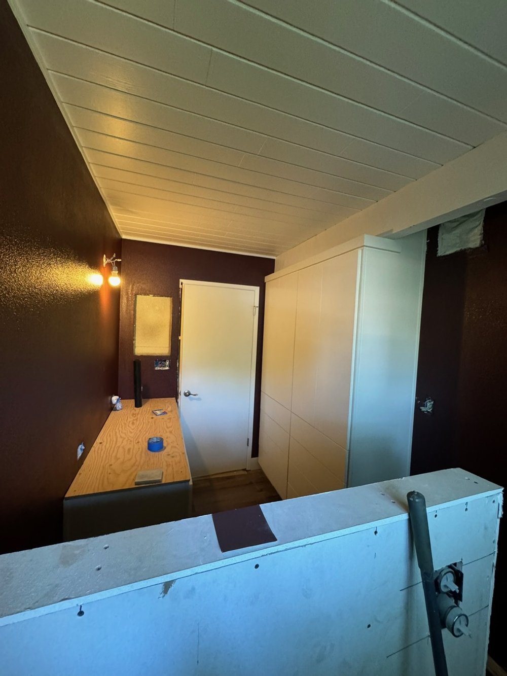 Room under renovation with a white cabinet, wooden countertop, dark purple walls, and construction tools.