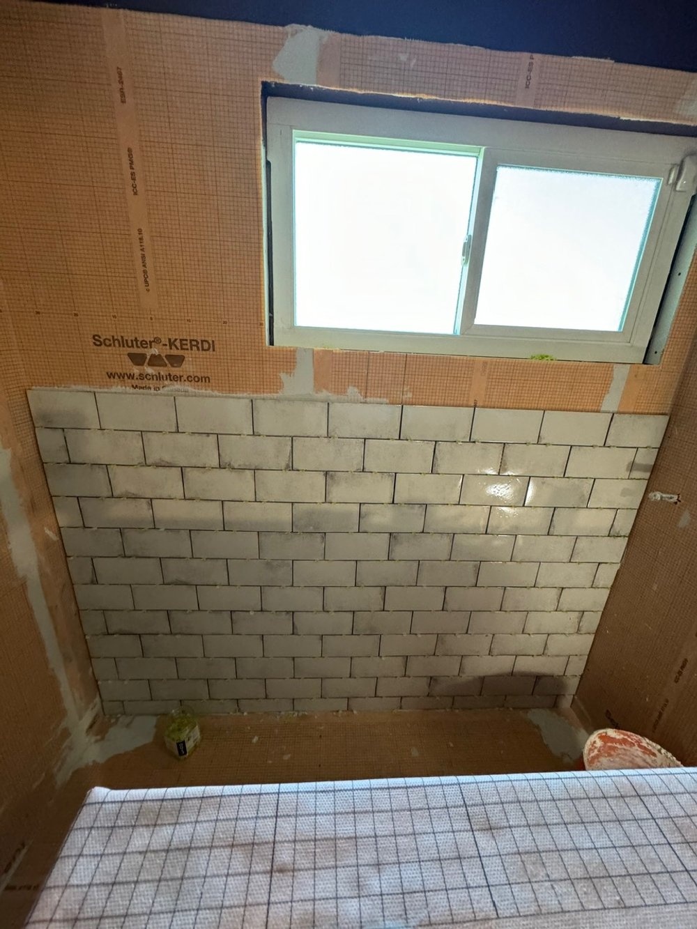 Interior of a room under construction with a small window, brick wall partially built, and construction materials on the floor.