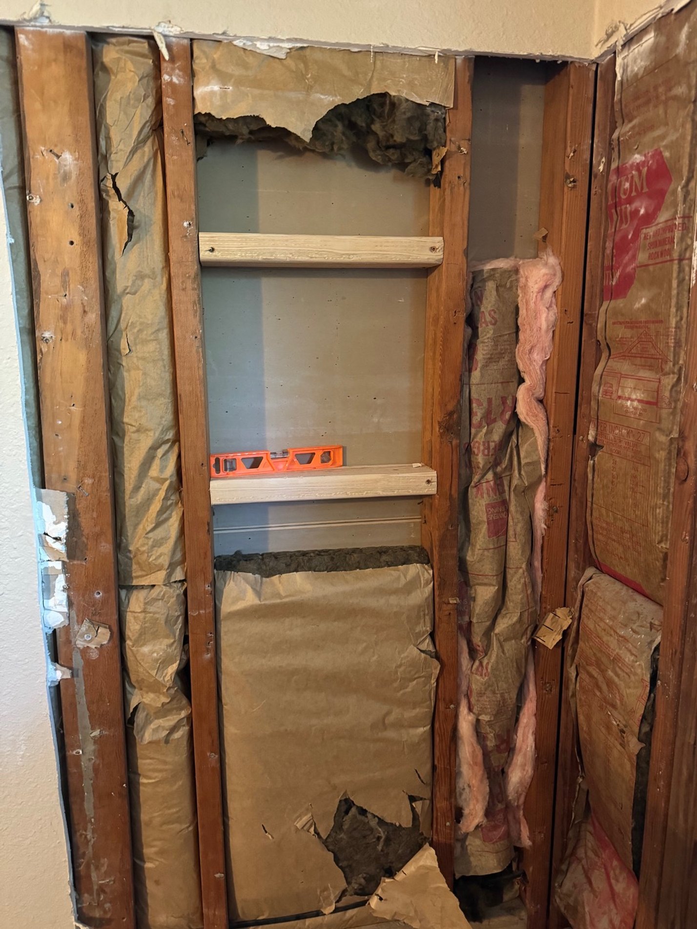 Wall showing exposed wooden studs, insulation, and damaged drywall in a renovation process.