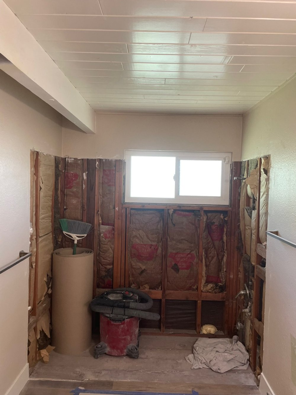 Room under renovation with exposed wall studs, insulation, a small window, and construction supplies.