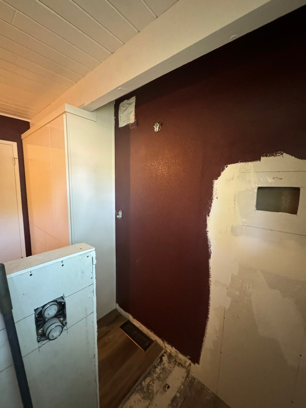 A bathroom under renovation with exposed pipes and partially painted walls, including a white cabinet and a brown painted accent wall.