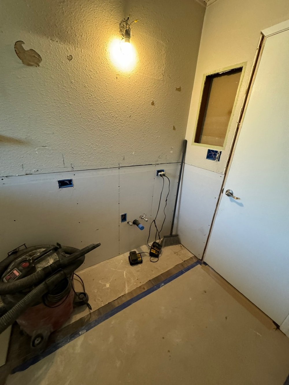 Room under renovation with exposed wall wiring, a wall with holes, a vacuum cleaner, and construction tools on the floor.