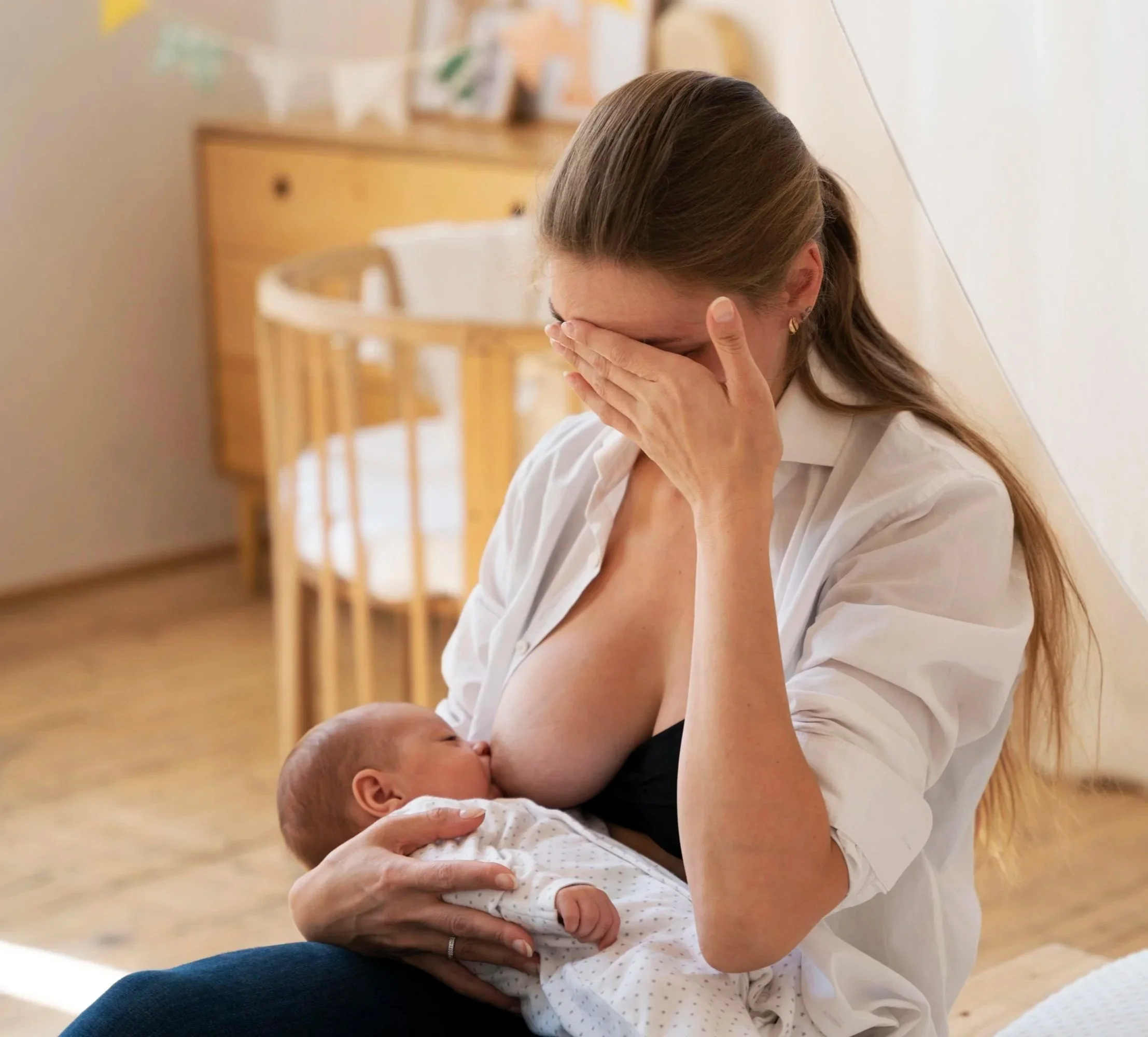 A baby girl with a lace bow headband breastfeeding, held securely by an adult's hand.