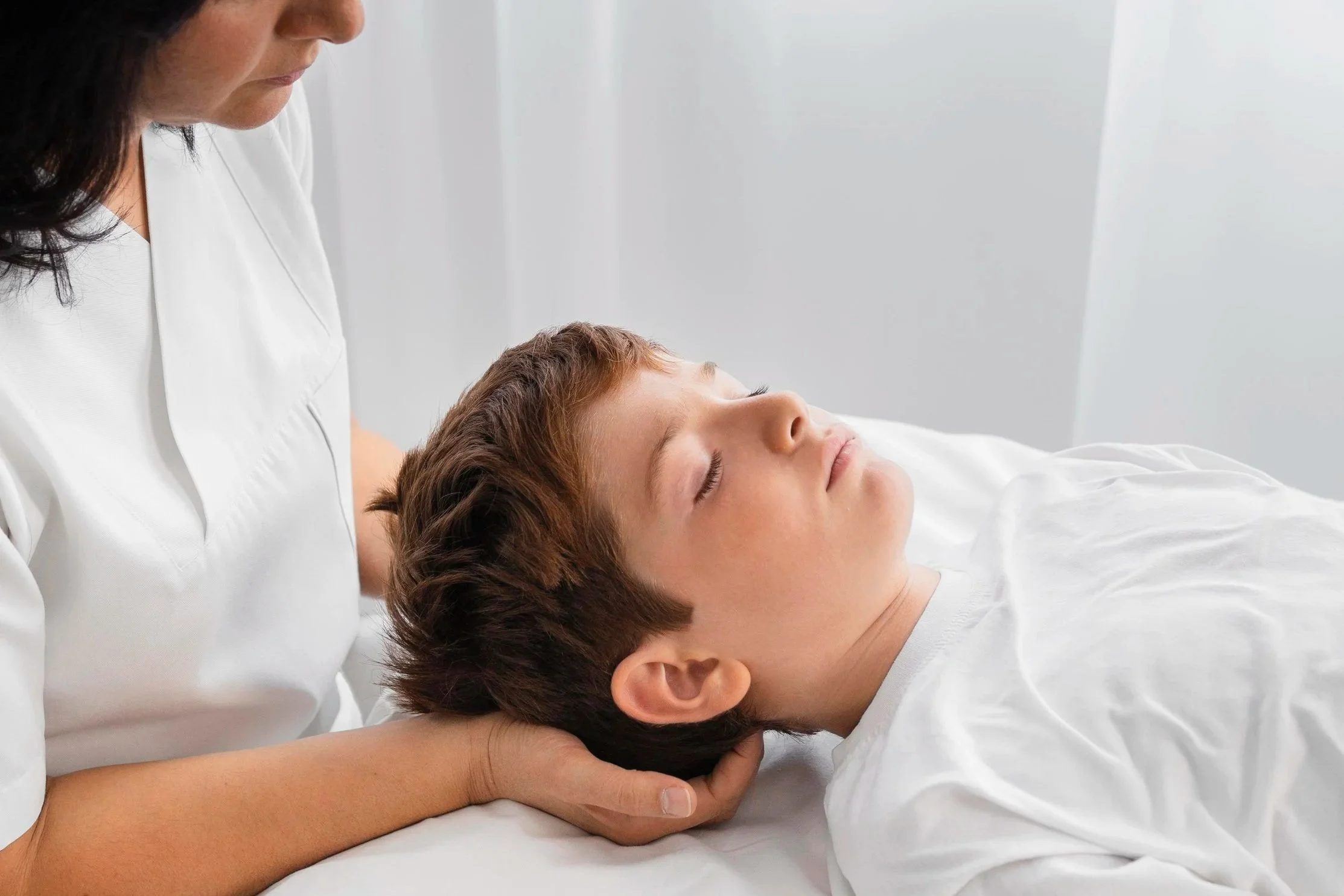 Close-up of a child's face with closed eyes, lying down on a bed, with soft lighting and a bokeh background.