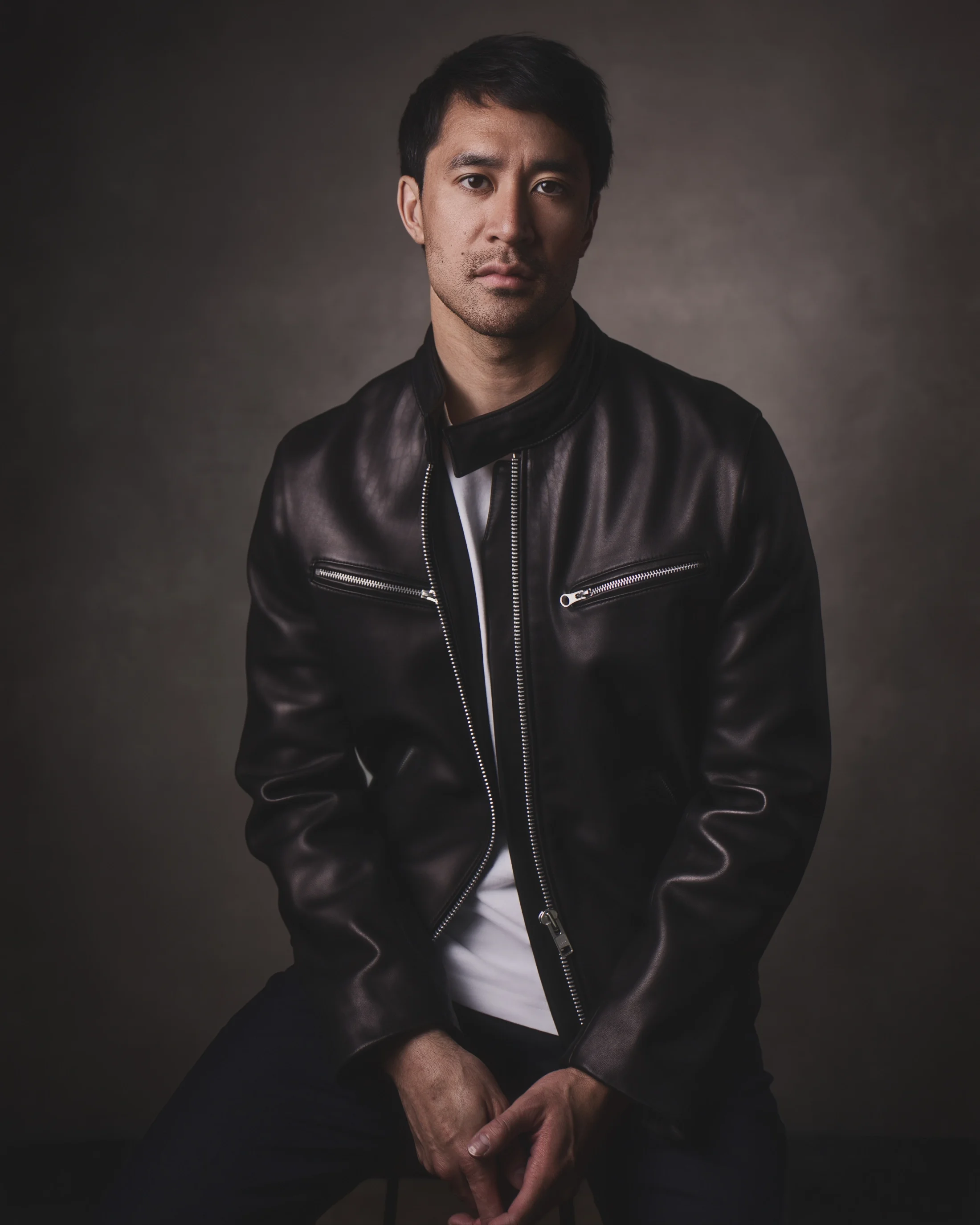 Moody portrait of a young Asian man wearing a black leather jacket and a white t-shirt