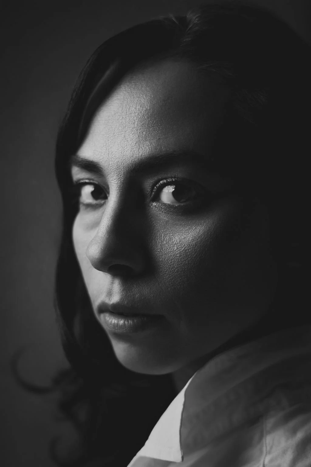 Black and white close-up portrait of a woman with dark, wavy hair and smooth skin, looking sadly into the camera.