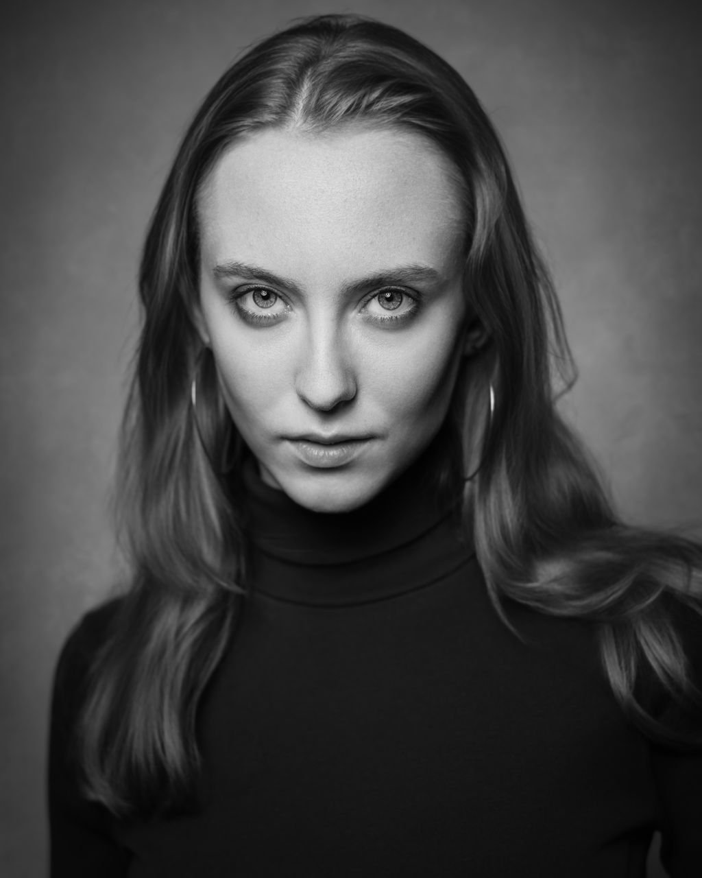 Black and white portrait of a young blonde woman with intense eyes staring into the camera while wearing a black turtleneck