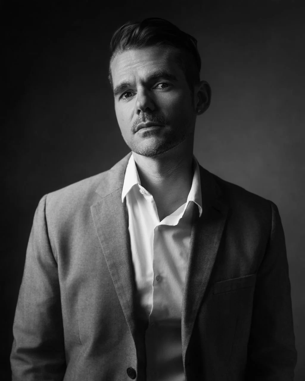 Black and white portrait of a man in a suit and white shirt, looking serious, against a dark background.
