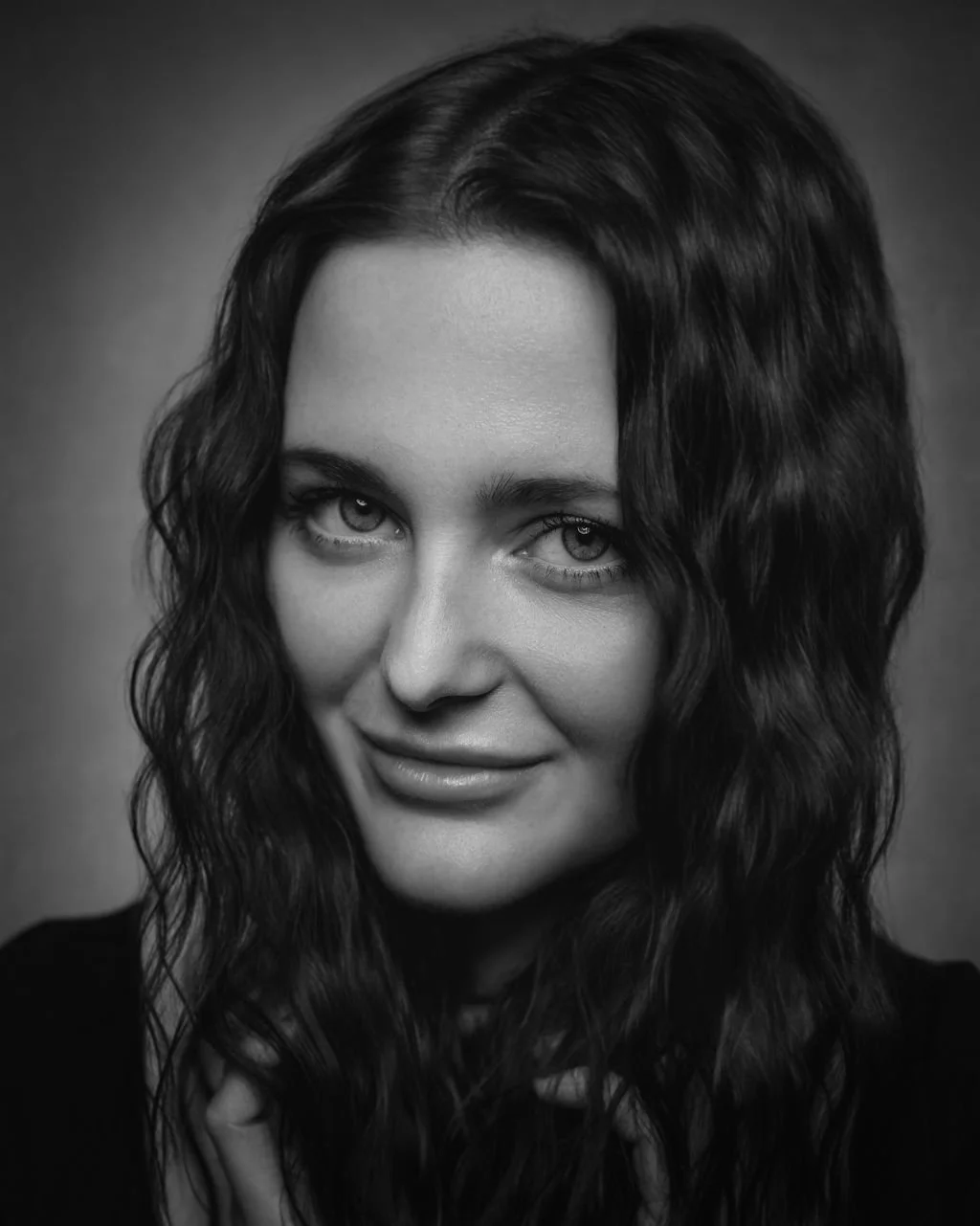  Black and white portrait of a woman with wavy hair and intense eyes, looking directly at the camera.
