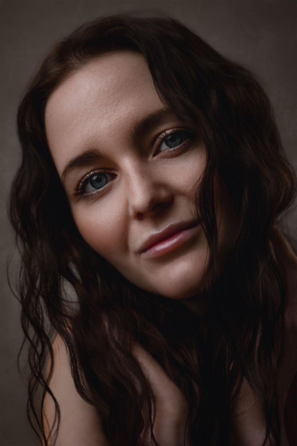 Close-up portrait of a woman with dark wavy hair and piercing blue eyes, smiling softly.