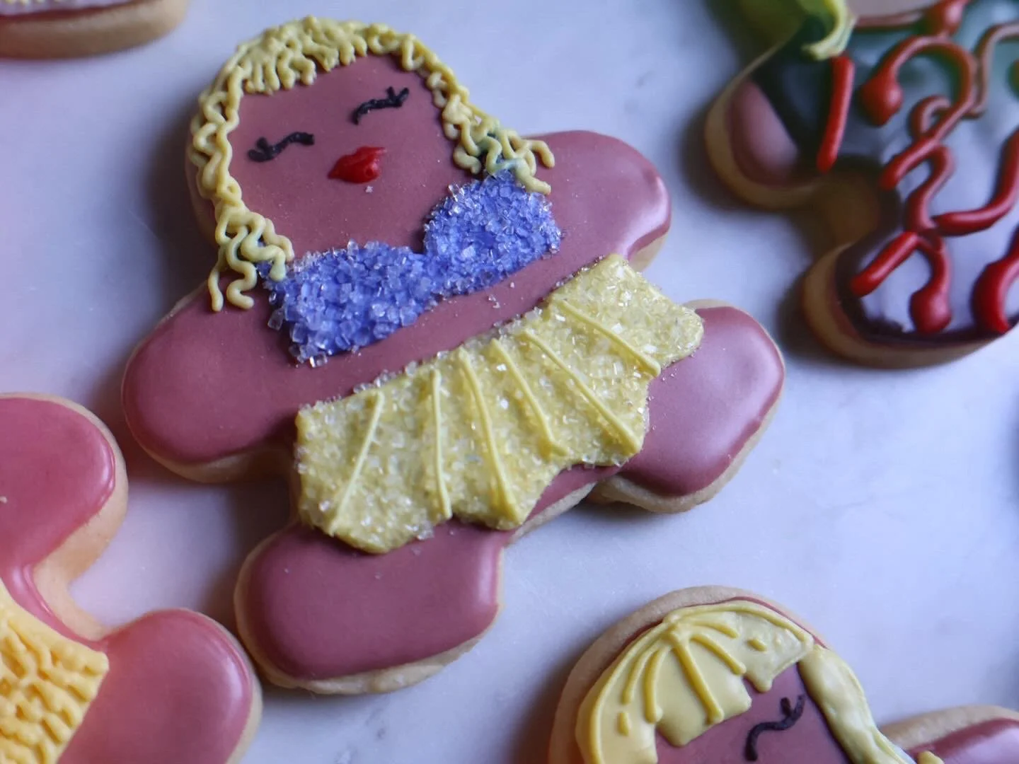 Decorated cookies shaped like a ballerina and other figures with pink, yellow, purple, and red icing.