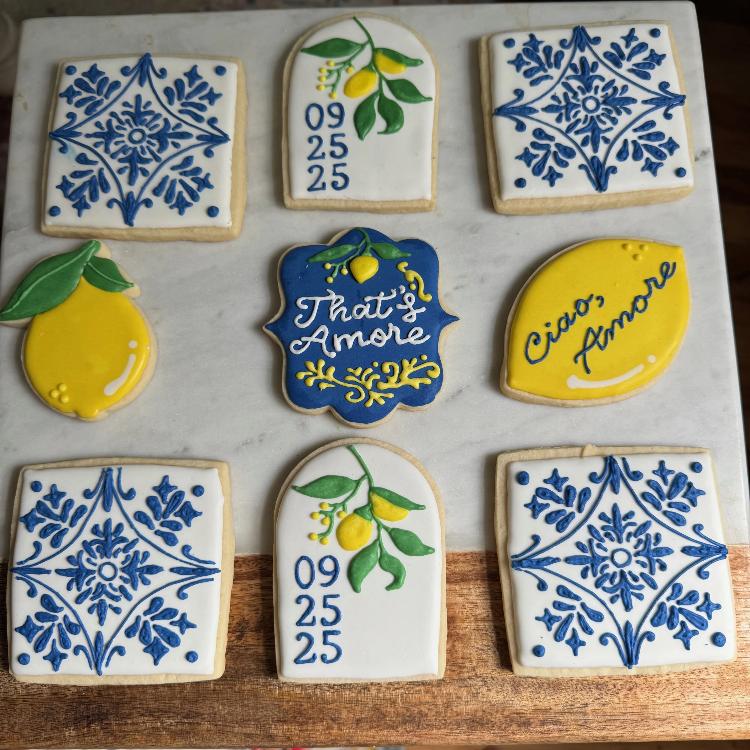 Decorative cookies with blue and yellow icing featuring floral patterns, lemons, dates, and romantic messages in Italian and Spanish.