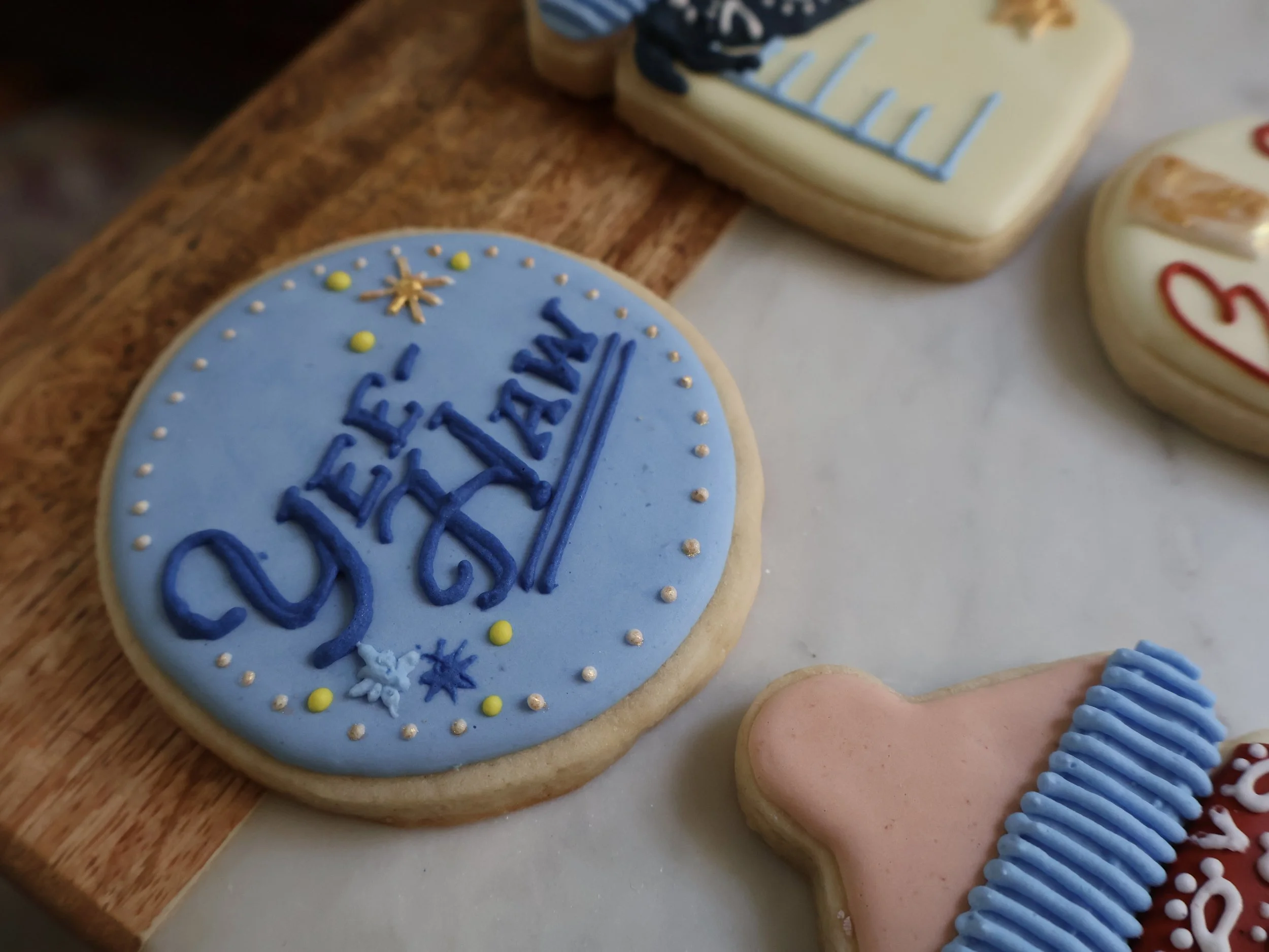 Decorated Christmas cookies on a wooden surface, including a round cookie with blue icing and the words "Come in" written on it, stars, and dots, along with other decorated cookies.
