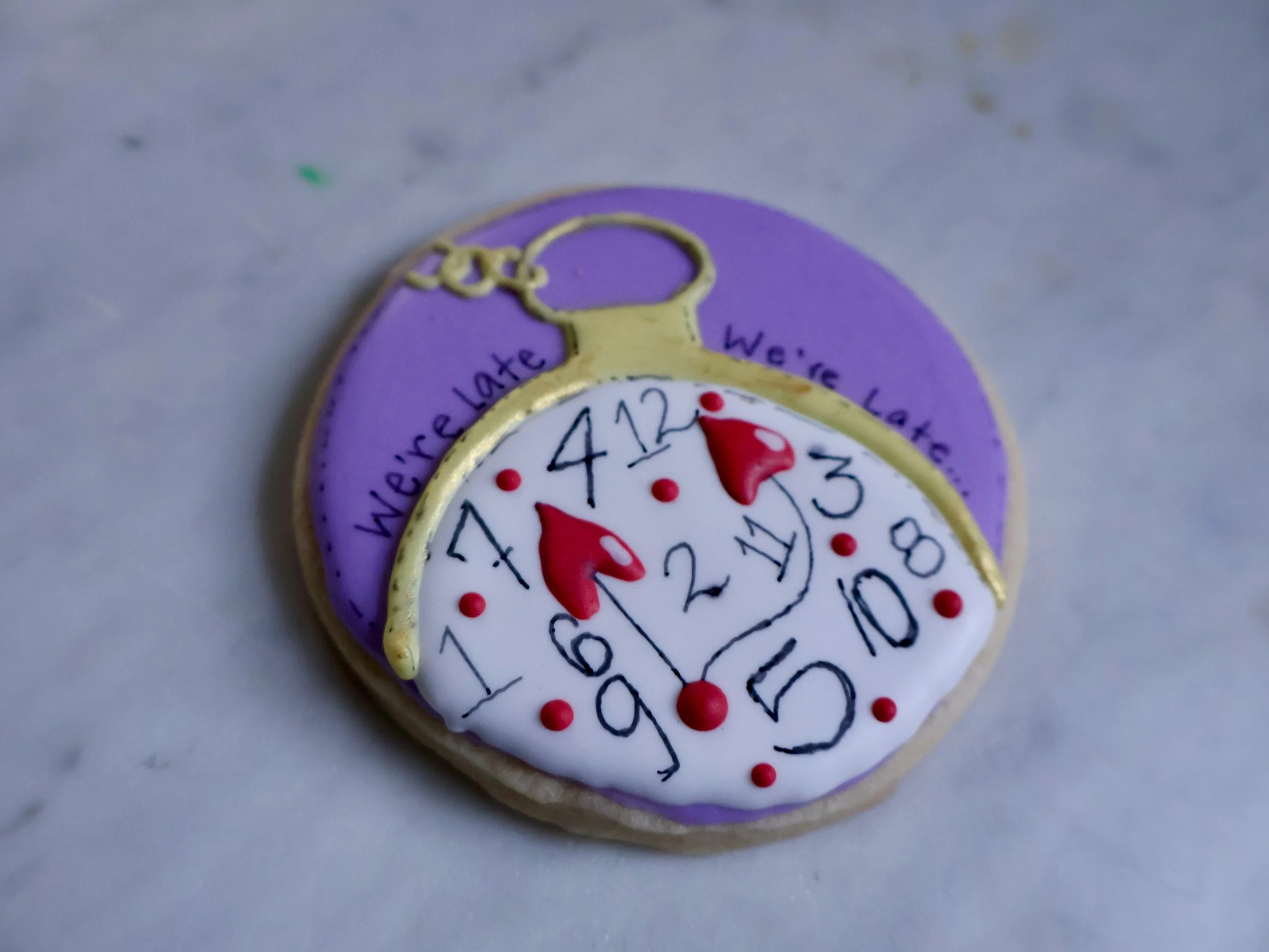 Decorative cookie shaped like a pocket watch with purple, white, red, and yellow icing details.