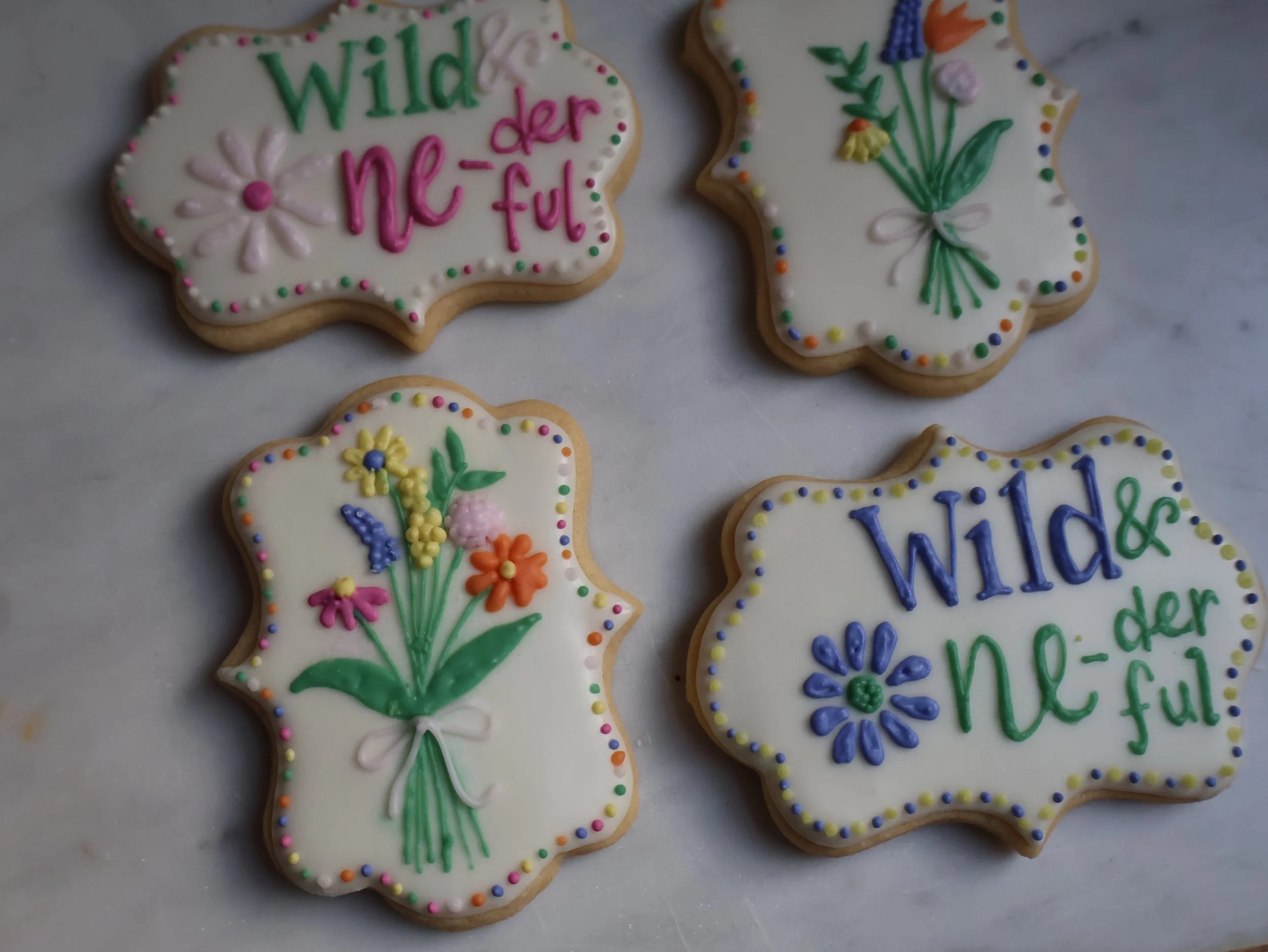Decorated cookies with floral and text designs on white icing, celebrating spring or a cheerful theme.