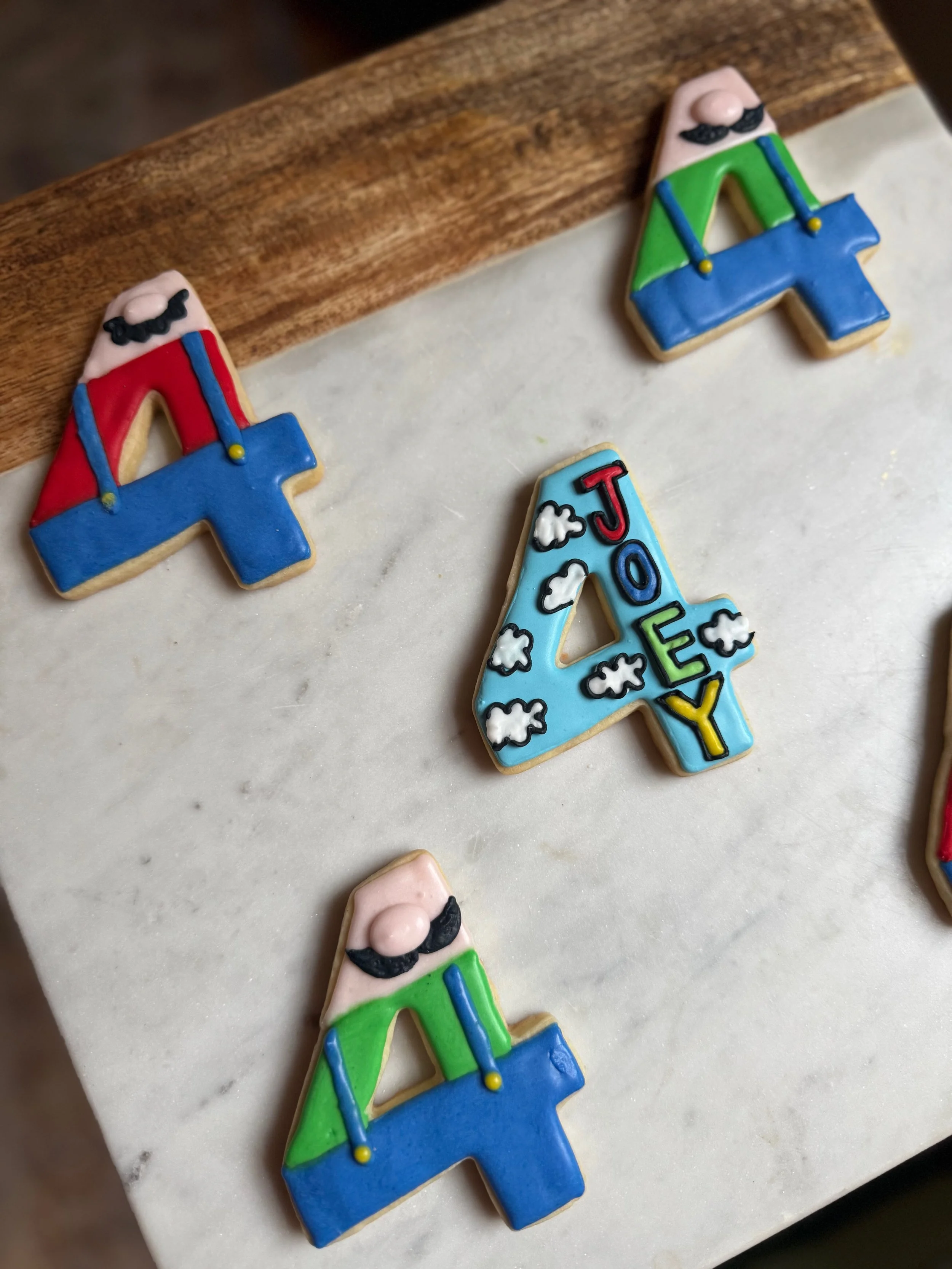 Colorful cookies decorated with Toy Story characters, including two with Woody's face and two with Buzz Lightyear's face, along with a letter 'A' cookie decorated with clouds and the name 'Joey'.
