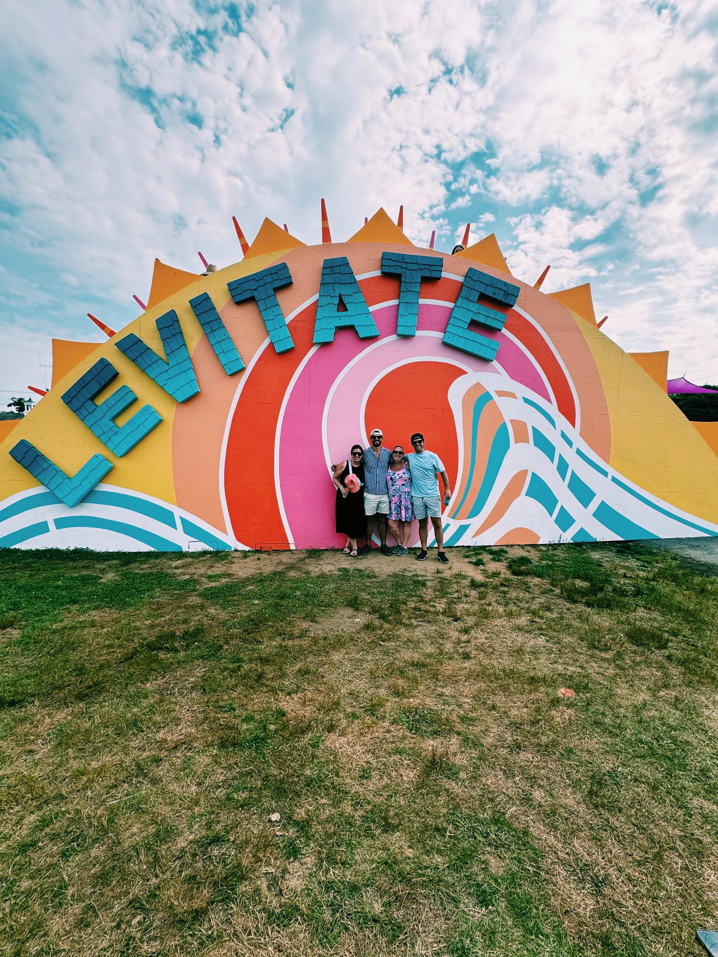 A colorful mural with the word 'LEVITATE' on it, featuring a wave design in pink, orange, white, and blue. There are four people standing in front of it.